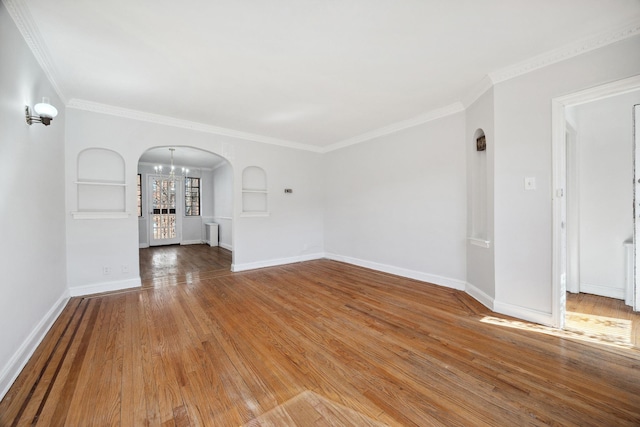 unfurnished living room with arched walkways, ornamental molding, hardwood / wood-style flooring, and baseboards