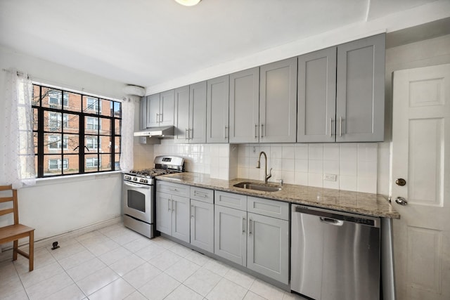 kitchen featuring stainless steel appliances, tasteful backsplash, a sink, and gray cabinetry