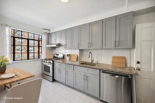 kitchen with stainless steel appliances, gray cabinets, a sink, and tasteful backsplash