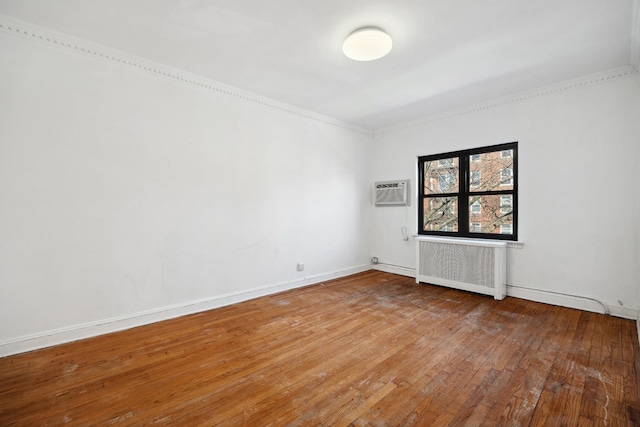 unfurnished room with baseboards, radiator heating unit, wood-type flooring, ornamental molding, and a wall mounted air conditioner