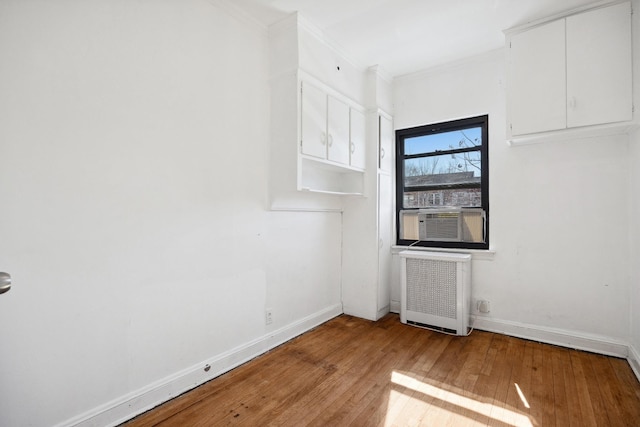 spare room featuring crown molding, baseboards, wood-type flooring, and radiator