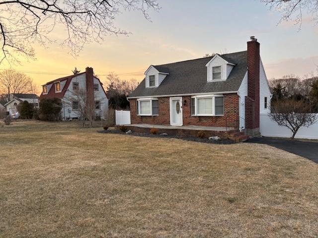 cape cod-style house with a chimney, a lawn, and brick siding