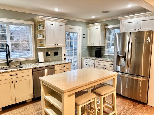 kitchen featuring appliances with stainless steel finishes, a sink, ornamental molding, and open shelves