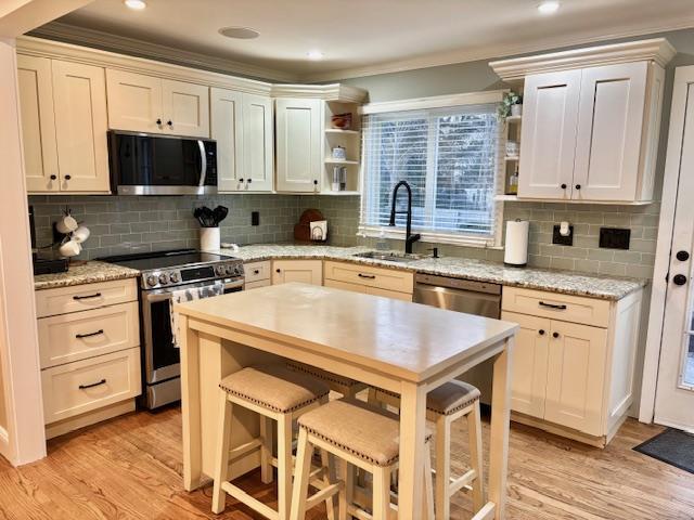 kitchen with stainless steel appliances, a sink, light wood-type flooring, backsplash, and open shelves