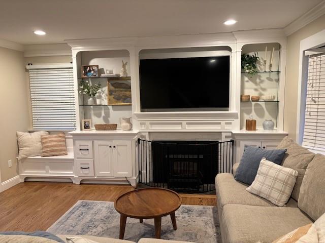 living area with recessed lighting, a fireplace, crown molding, and light wood finished floors