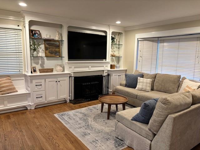 living area featuring a fireplace with flush hearth, recessed lighting, crown molding, and wood finished floors