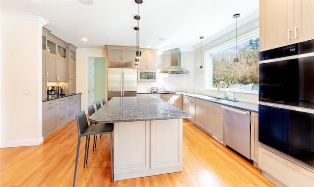 kitchen with ornamental molding, a center island, built in appliances, wall chimney range hood, and a sink