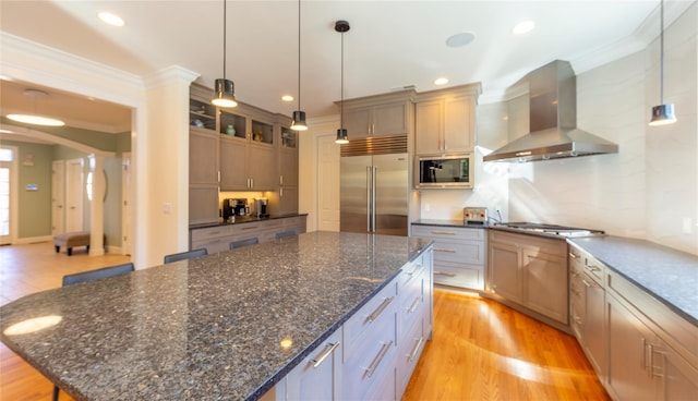 kitchen with built in appliances, arched walkways, a spacious island, wall chimney range hood, and ornamental molding