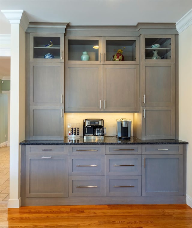 bar featuring ornate columns, ornamental molding, light wood-type flooring, and baseboards