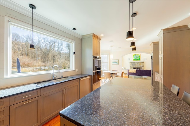 kitchen featuring decorative light fixtures, open floor plan, a sink, a stone fireplace, and dark stone counters