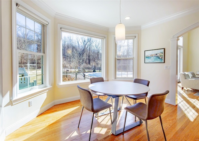 dining space with baseboards, ornate columns, light wood-style flooring, and crown molding