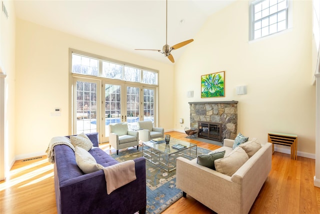 living room featuring a healthy amount of sunlight, light wood-style flooring, high vaulted ceiling, and a stone fireplace