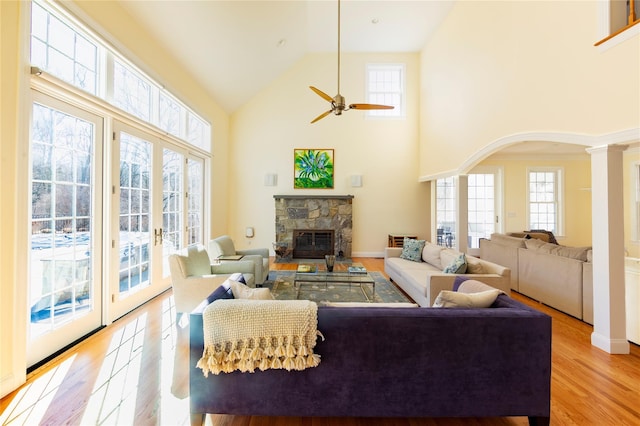 living room with arched walkways, high vaulted ceiling, a fireplace, light wood finished floors, and decorative columns