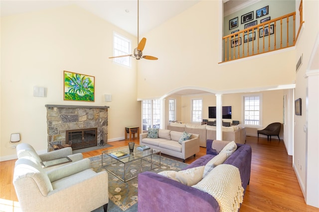 living room featuring visible vents, ceiling fan, a stone fireplace, wood finished floors, and ornate columns