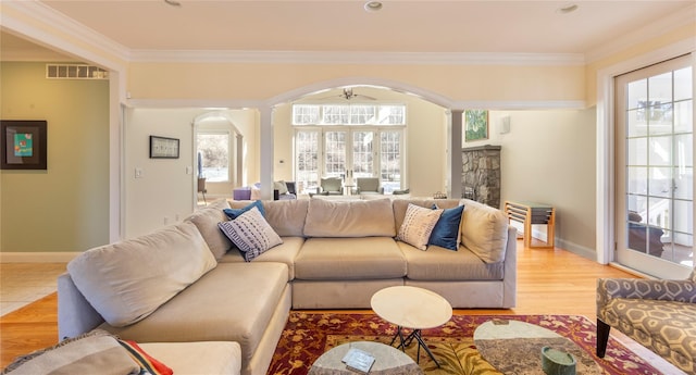 living room with arched walkways, light wood-style flooring, visible vents, baseboards, and crown molding