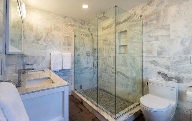 full bathroom with double vanity, toilet, a sink, a shower stall, and tile walls