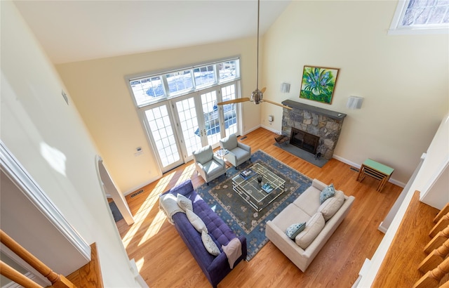 living room featuring visible vents, a stone fireplace, wood finished floors, high vaulted ceiling, and baseboards