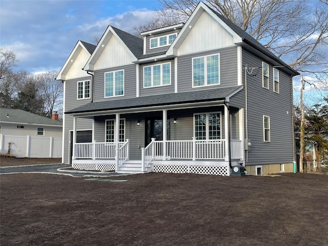 view of front facade with a porch, a shingled roof, board and batten siding, fence, and driveway