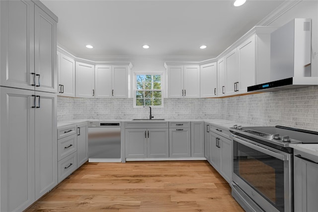 kitchen with a sink, stainless steel range with electric stovetop, light countertops, and wall chimney range hood