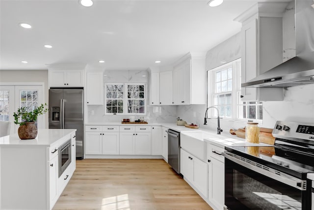 kitchen with wall chimney range hood, appliances with stainless steel finishes, light countertops, and a sink