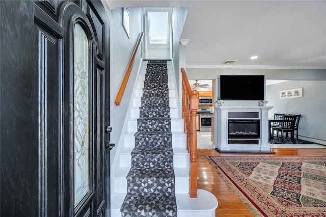 foyer featuring crown molding, visible vents, stairway, a glass covered fireplace, and wood finished floors