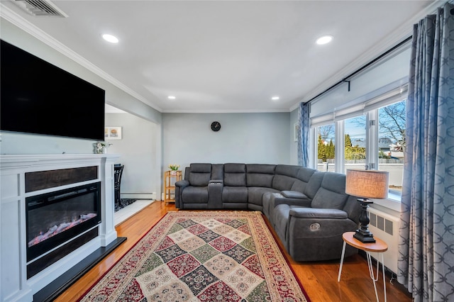 living room with visible vents, a glass covered fireplace, light wood-style flooring, ornamental molding, and a baseboard heating unit