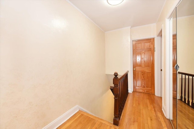 corridor featuring an upstairs landing, light wood-style flooring, crown molding, and baseboards