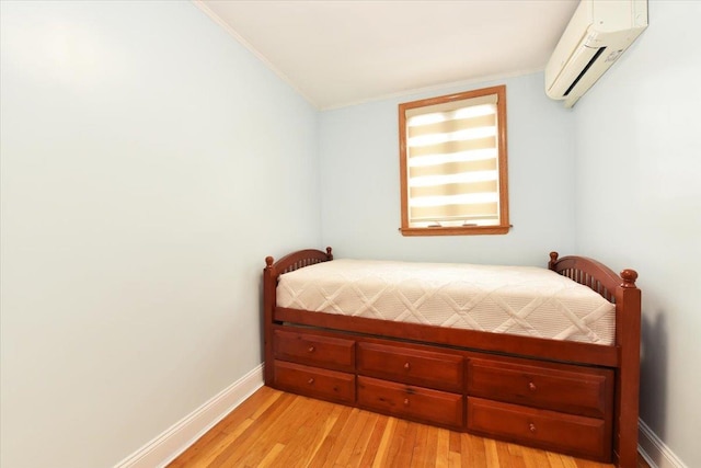 bedroom featuring an AC wall unit, baseboards, light wood finished floors, and ornamental molding