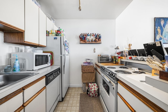 kitchen featuring light floors, light countertops, white cabinets, white appliances, and baseboards