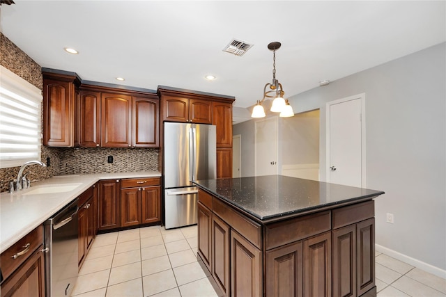 kitchen featuring stainless steel appliances, a sink, visible vents, decorative backsplash, and decorative light fixtures