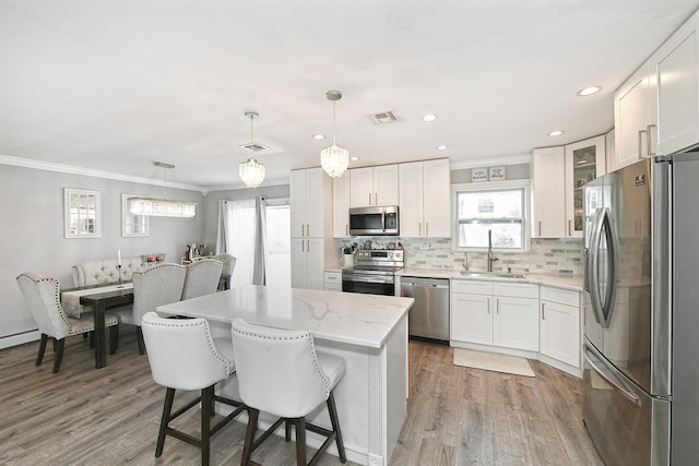 kitchen featuring stainless steel appliances, a sink, visible vents, backsplash, and a center island