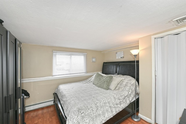 bedroom with dark wood-type flooring, a baseboard radiator, visible vents, and a textured ceiling