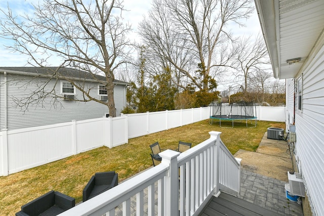 wooden deck featuring central air condition unit, a fenced backyard, a trampoline, and a yard