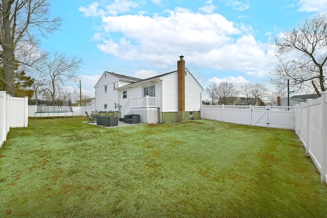 back of house with a fenced backyard, a trampoline, a gate, and a lawn