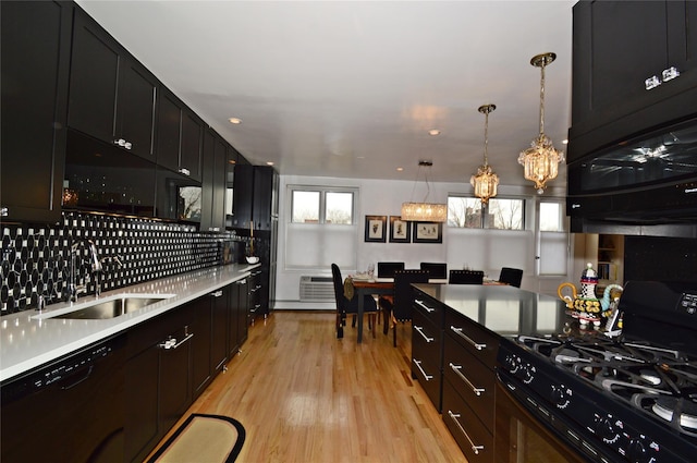 kitchen with decorative backsplash, light countertops, light wood-type flooring, black appliances, and a sink