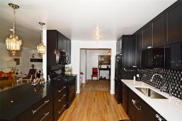 kitchen with hanging light fixtures, light wood-style flooring, an inviting chandelier, a sink, and black appliances