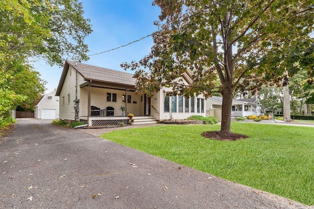 view of front of home featuring driveway, covered porch, a detached garage, and a front lawn