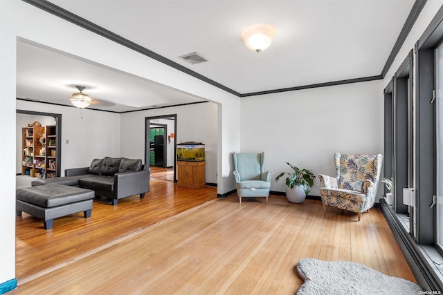 living room with light wood-style flooring, visible vents, baseboards, and ornamental molding