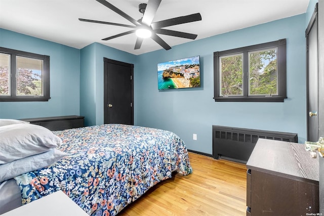 bedroom featuring a ceiling fan, radiator, baseboards, and light wood finished floors