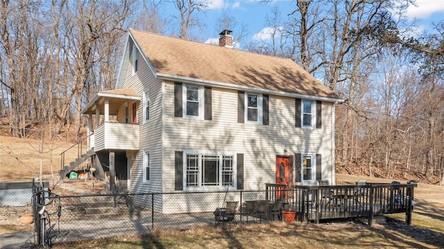 view of front facade featuring a fenced front yard, roof with shingles, a chimney, a wooden deck, and stairs