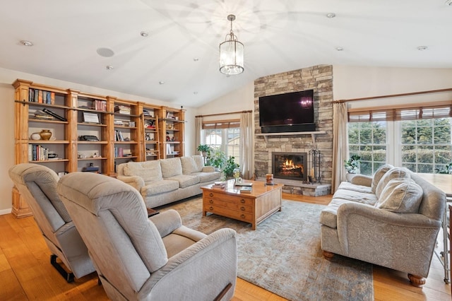 living room featuring a fireplace, vaulted ceiling, light wood-style flooring, and a notable chandelier