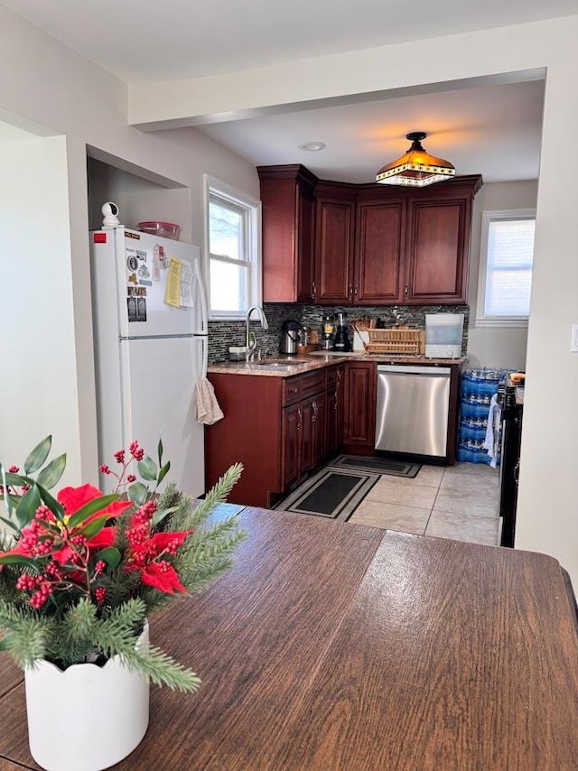 kitchen with a sink, a healthy amount of sunlight, stainless steel dishwasher, freestanding refrigerator, and decorative backsplash