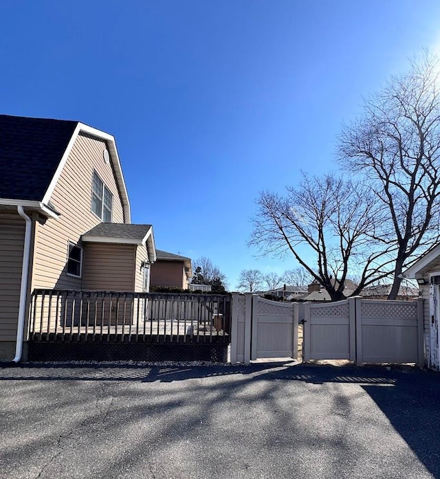 view of side of property with a shingled roof and a gate