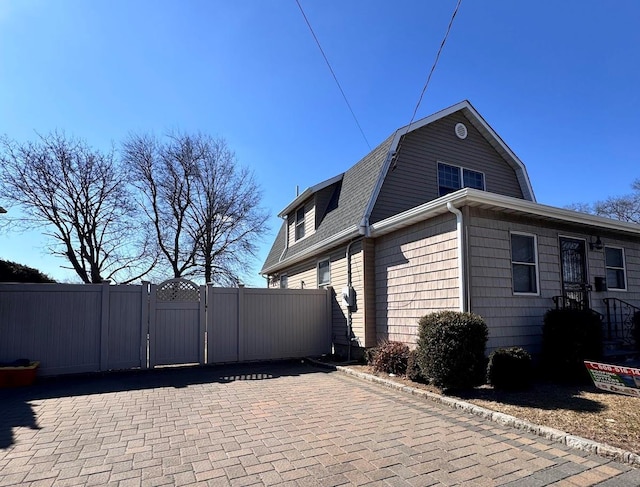 view of side of property with a shingled roof, a gate, fence, and a gambrel roof