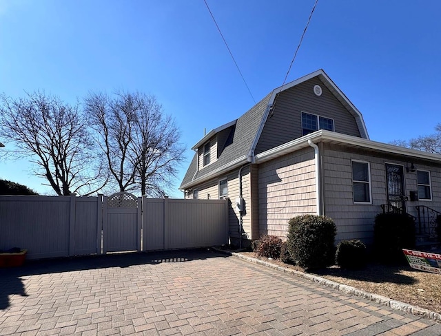 view of side of home with a gambrel roof, fence, roof with shingles, and a gate