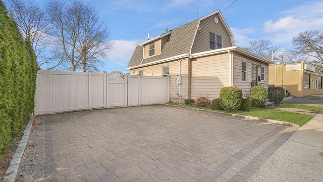 view of home's exterior featuring a gambrel roof, fence, roof with shingles, and a gate