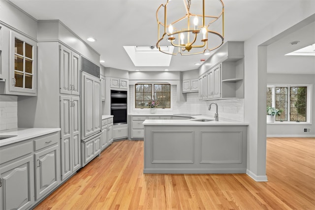 kitchen featuring a skylight, light countertops, gray cabinetry, stainless steel double oven, and a sink