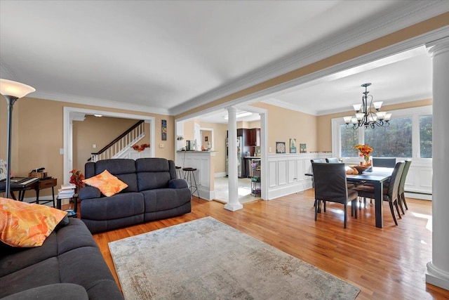 living room with a wainscoted wall, crown molding, light wood finished floors, a baseboard radiator, and ornate columns