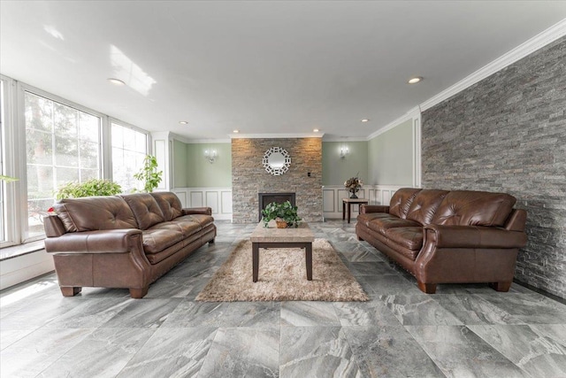 living room with a stone fireplace, a wainscoted wall, crown molding, and a decorative wall