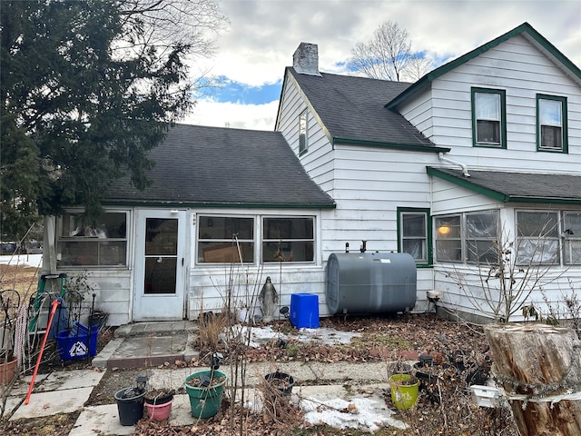 back of property featuring heating fuel, a chimney, and roof with shingles